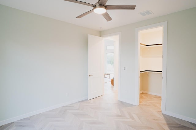 unfurnished bedroom featuring a spacious closet, a closet, ceiling fan, and light parquet flooring