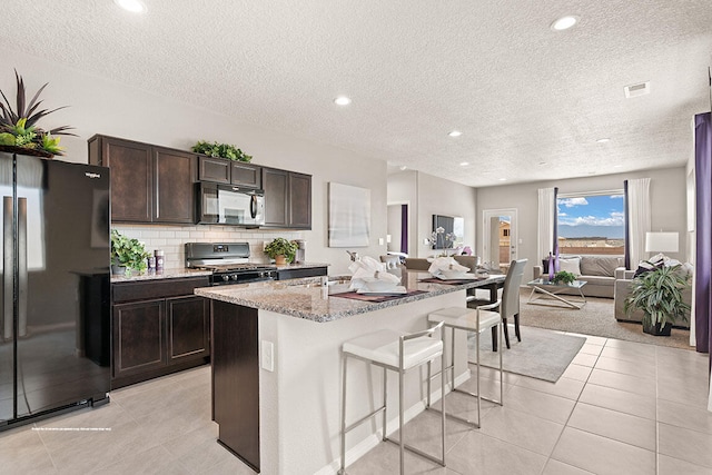 kitchen with a breakfast bar, black appliances, decorative backsplash, an island with sink, and a textured ceiling