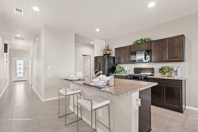 kitchen featuring black appliances, a center island with sink, dark brown cabinetry, and a textured ceiling