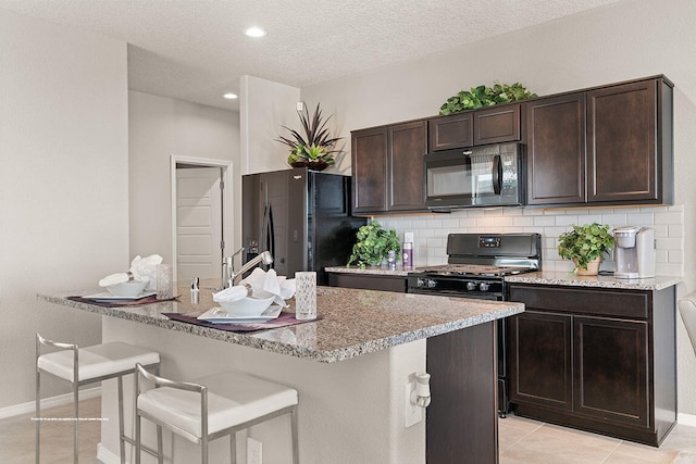 kitchen featuring dark brown cabinetry, tasteful backsplash, a textured ceiling, a breakfast bar area, and black appliances