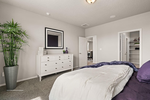 bedroom featuring a textured ceiling, a walk in closet, dark carpet, and a closet