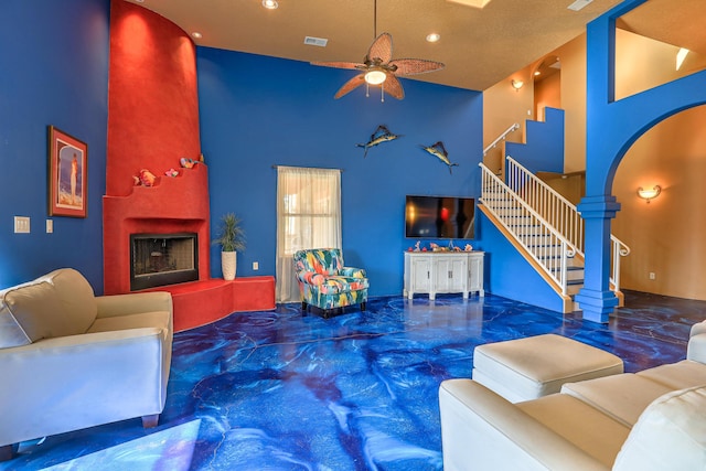 living room featuring ceiling fan, a tile fireplace, a textured ceiling, and high vaulted ceiling