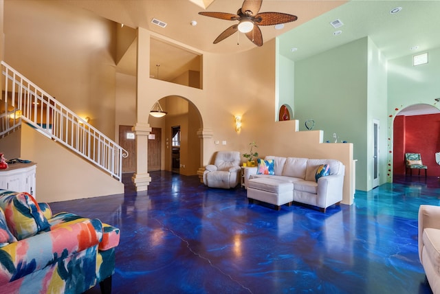 living room with stairs, arched walkways, a ceiling fan, and ornate columns