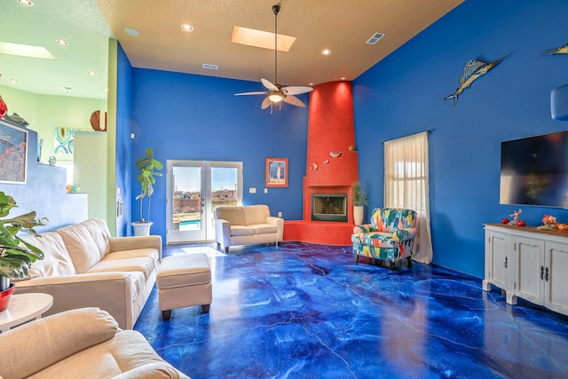 living room featuring a high ceiling, a skylight, ceiling fan, a textured ceiling, and a large fireplace