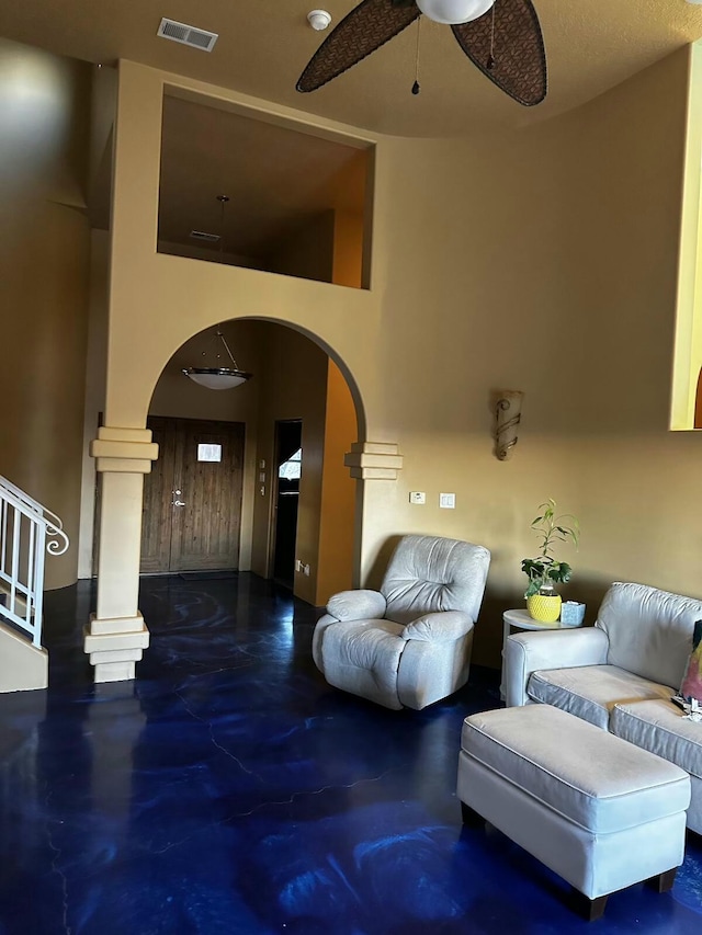 living area with arched walkways, finished concrete flooring, visible vents, ceiling fan, and ornate columns