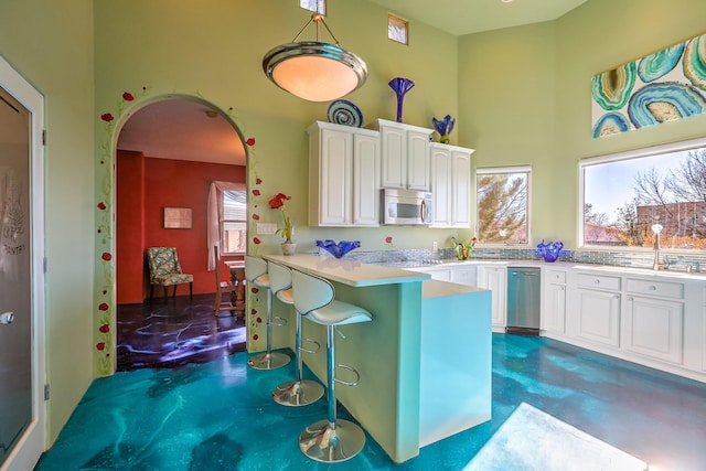 kitchen featuring arched walkways, stainless steel microwave, a towering ceiling, concrete flooring, and a peninsula