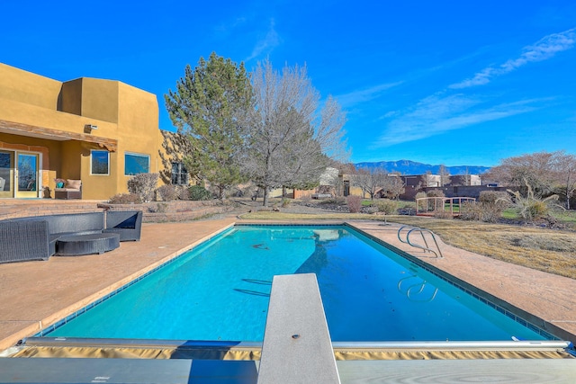 view of swimming pool with a patio, a mountain view, an outdoor living space, a diving board, and a fenced in pool