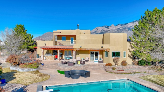 rear view of house featuring an outdoor pool, a balcony, a patio area, a mountain view, and stucco siding