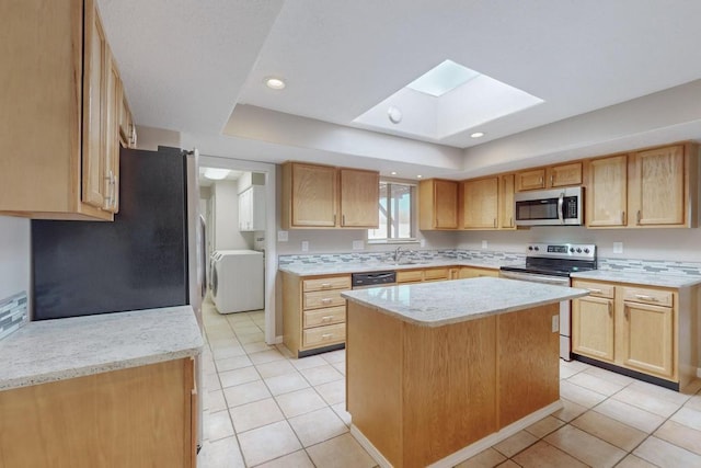 kitchen with a skylight, a center island, stainless steel appliances, washer / dryer, and light tile patterned floors