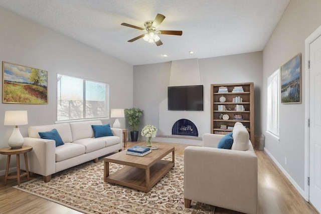 living room with a fireplace, ceiling fan, and light hardwood / wood-style flooring