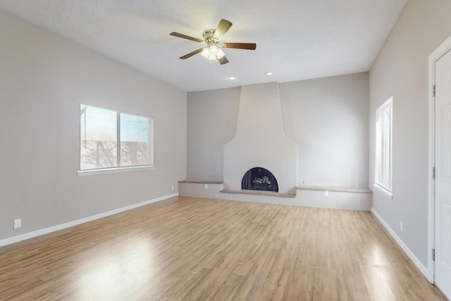 unfurnished living room featuring ceiling fan, a fireplace, and light wood-type flooring