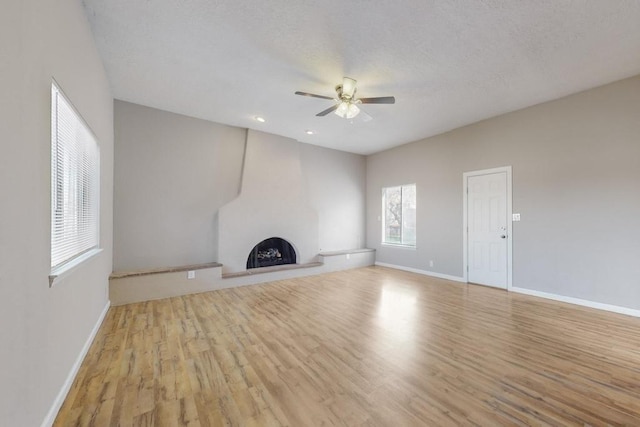 unfurnished living room with a textured ceiling, ceiling fan, light hardwood / wood-style floors, and a fireplace