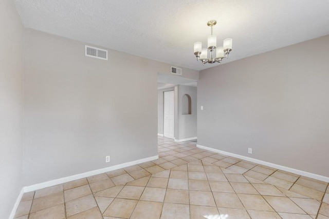 tiled empty room with a chandelier and a textured ceiling