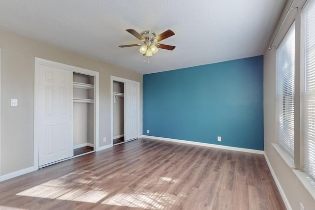 unfurnished bedroom with wood-type flooring, ceiling fan, and multiple closets