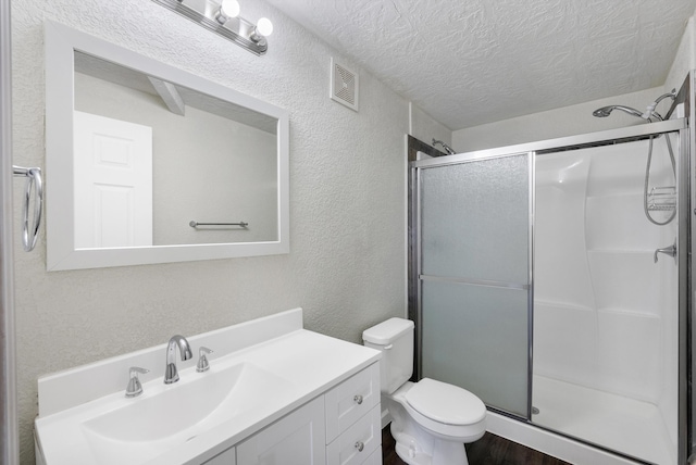 bathroom featuring vanity, toilet, a shower with door, and a textured ceiling