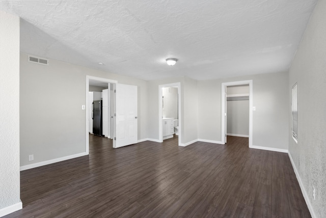 unfurnished bedroom featuring black fridge, a textured ceiling, a spacious closet, connected bathroom, and dark hardwood / wood-style floors