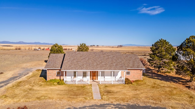 view of front facade featuring a mountain view, a front lawn, covered porch, and a rural view