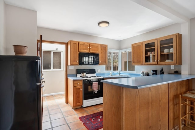 kitchen featuring a kitchen breakfast bar, black appliances, a peninsula, brown cabinetry, and glass insert cabinets