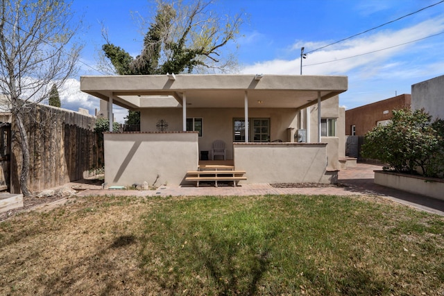 back of house with stucco siding, fence, and a yard
