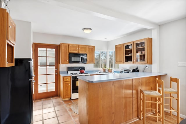 kitchen featuring kitchen peninsula, light tile patterned floors, a kitchen bar, and black appliances