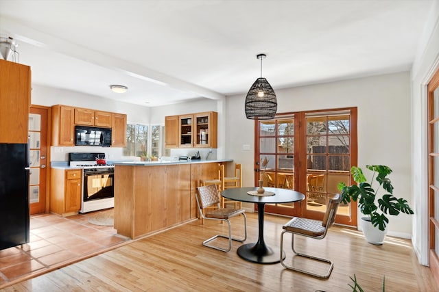 kitchen with a wealth of natural light, kitchen peninsula, pendant lighting, light hardwood / wood-style floors, and black appliances