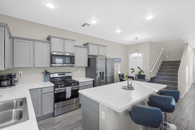 kitchen with pendant lighting, an inviting chandelier, light wood-type flooring, a kitchen island, and stainless steel appliances