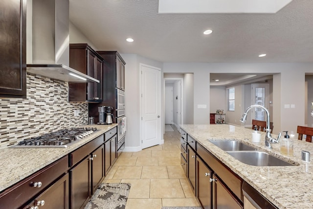 kitchen featuring light stone counters, sink, wall chimney exhaust hood, and stainless steel appliances