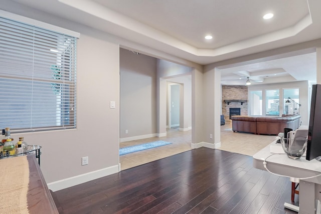 interior space featuring hardwood / wood-style flooring, a raised ceiling, ceiling fan, and a stone fireplace