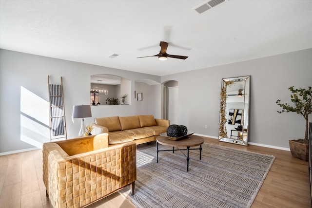 living room with ceiling fan with notable chandelier and light wood-type flooring