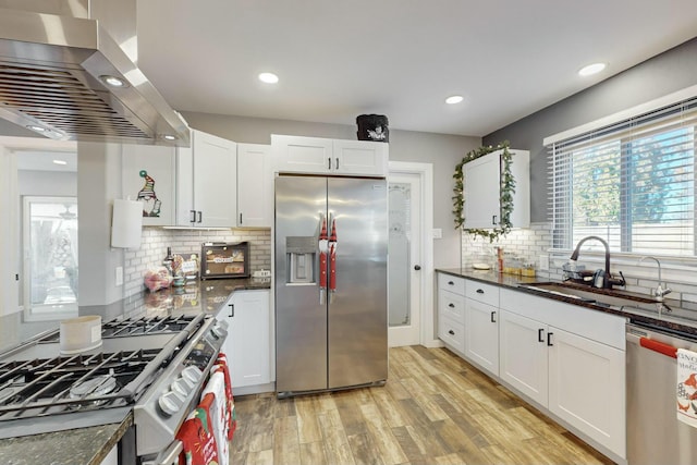 kitchen featuring light wood-type flooring, wall chimney exhaust hood, stainless steel appliances, sink, and white cabinetry