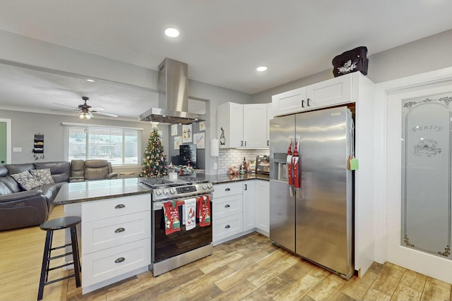 kitchen featuring kitchen peninsula, a kitchen bar, island range hood, white cabinets, and appliances with stainless steel finishes