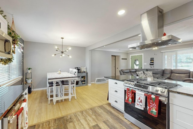 kitchen with white cabinetry, stainless steel gas range oven, a notable chandelier, ventilation hood, and light wood-type flooring