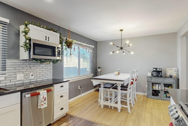 kitchen with light wood-type flooring, appliances with stainless steel finishes, tasteful backsplash, a notable chandelier, and white cabinetry