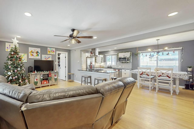 living room with ceiling fan with notable chandelier, light hardwood / wood-style floors, and sink