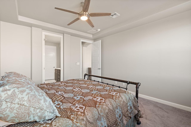 carpeted bedroom with ensuite bathroom, a raised ceiling, and ceiling fan