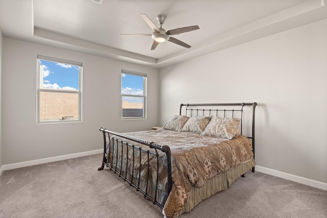 carpeted bedroom with ceiling fan and a tray ceiling