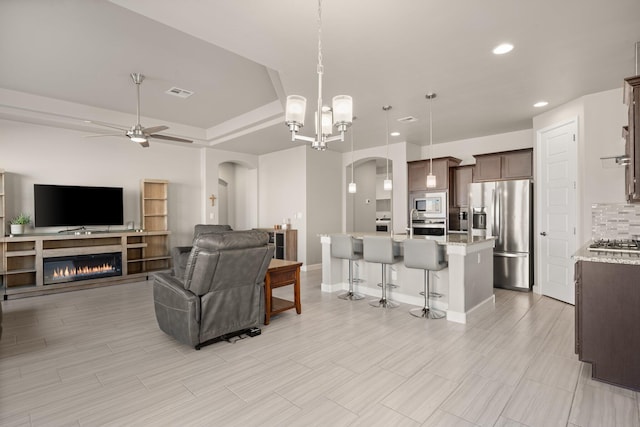 living room with ceiling fan with notable chandelier and a tray ceiling