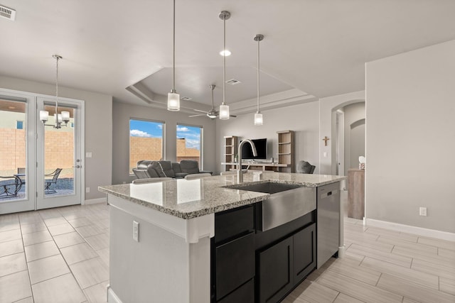 kitchen featuring dishwasher, a kitchen island with sink, pendant lighting, a tray ceiling, and sink