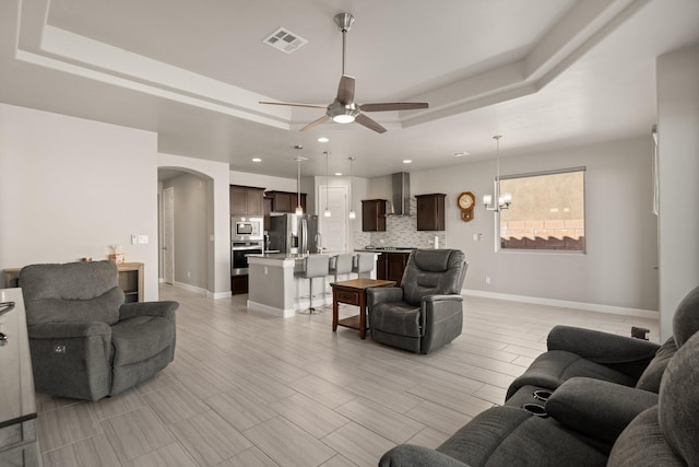 living room featuring ceiling fan with notable chandelier and a tray ceiling