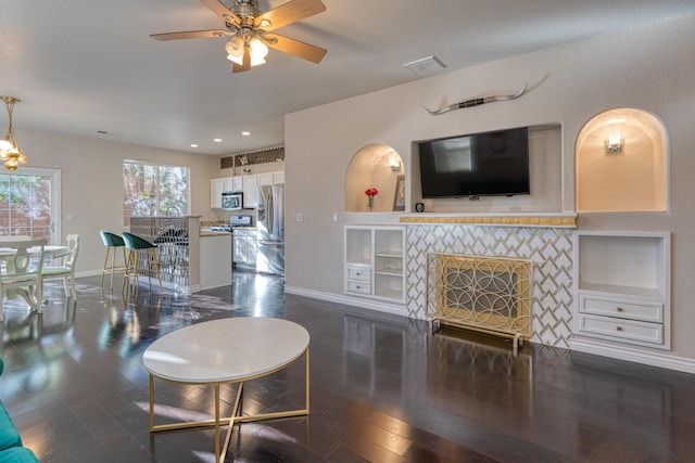 living room featuring built in shelves, ceiling fan, dark hardwood / wood-style flooring, and a tile fireplace