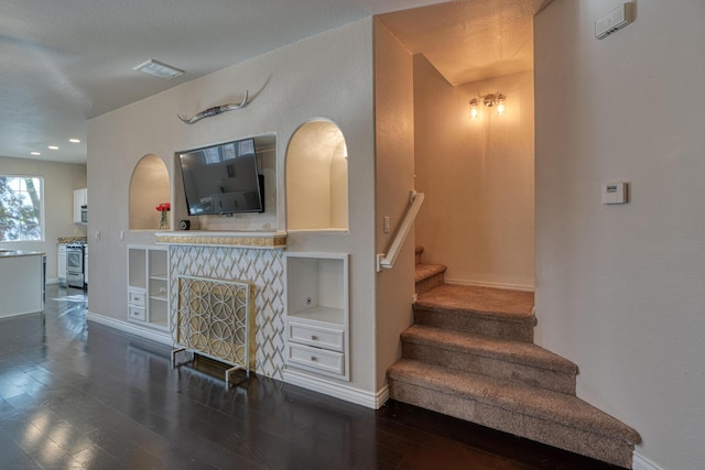 staircase with wood-type flooring, built in features, and a textured ceiling