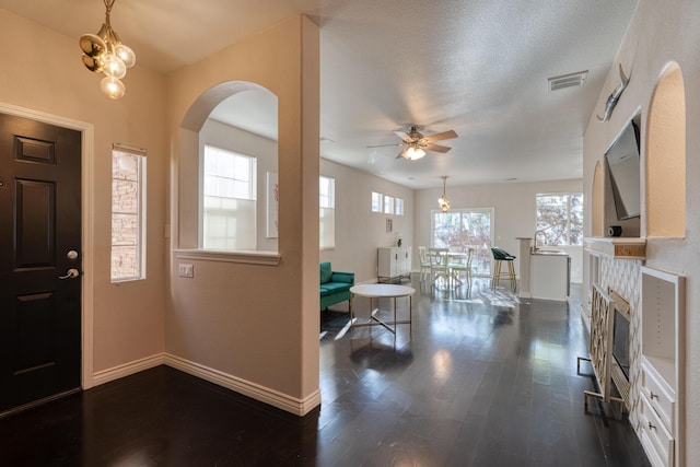 entryway featuring dark hardwood / wood-style flooring, ceiling fan with notable chandelier, a textured ceiling, and a tiled fireplace