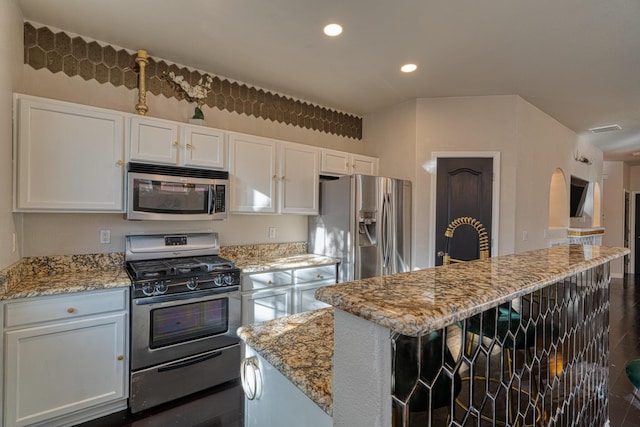 kitchen featuring stainless steel appliances, a kitchen island, white cabinetry, and light stone counters