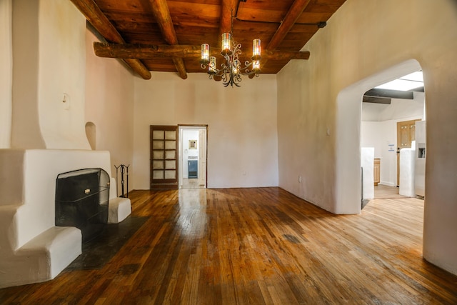 unfurnished living room featuring arched walkways, wooden ceiling, a notable chandelier, wood finished floors, and beam ceiling