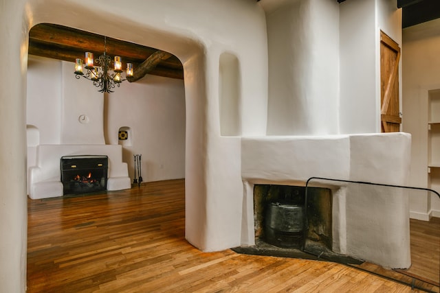 unfurnished living room featuring a fireplace, a chandelier, wood finished floors, and beamed ceiling