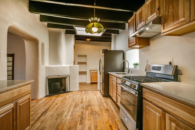 kitchen with a barn door, light brown cabinets, stainless steel gas stove, light hardwood / wood-style flooring, and sink