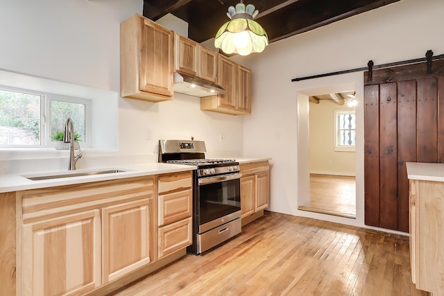 kitchen featuring a barn door, under cabinet range hood, a sink, light countertops, and stainless steel range with gas cooktop