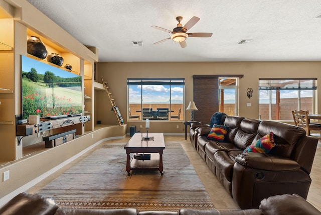 living room featuring ceiling fan, a textured ceiling, a wealth of natural light, and built in shelves