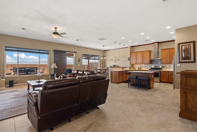 living room featuring ceiling fan with notable chandelier, sink, light tile patterned floors, and a textured ceiling