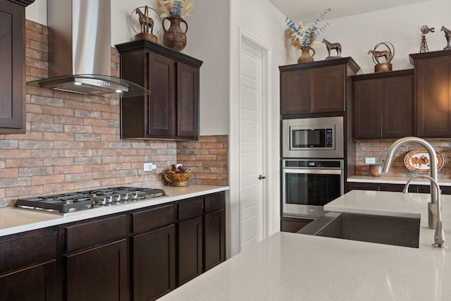 kitchen featuring stainless steel appliances, backsplash, a sink, dark brown cabinets, and wall chimney exhaust hood